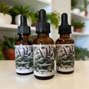 May include: Three amber glass bottles of Patchouli Diffusion Oil with black droppers. Each bottle has a white label with a botanical design of purple flowers and green leaves. The labels also include the text "Patchouli Diffusion Oil 1 oz / 30 ml".