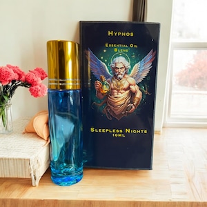 May include: A blue glass bottle with a gold cap and a label that reads "Hypnos Essential Oil Blend Sleepless Nights 10mL". The bottle is next to a box with a similar label and an illustration of a winged man holding a bottle.