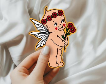 May include: A sticker of a cartoon cherub with wings, a flower crown, and a flower in its hand. The cherub has red cheeks and hearts for eyes. The sticker is on a white background.