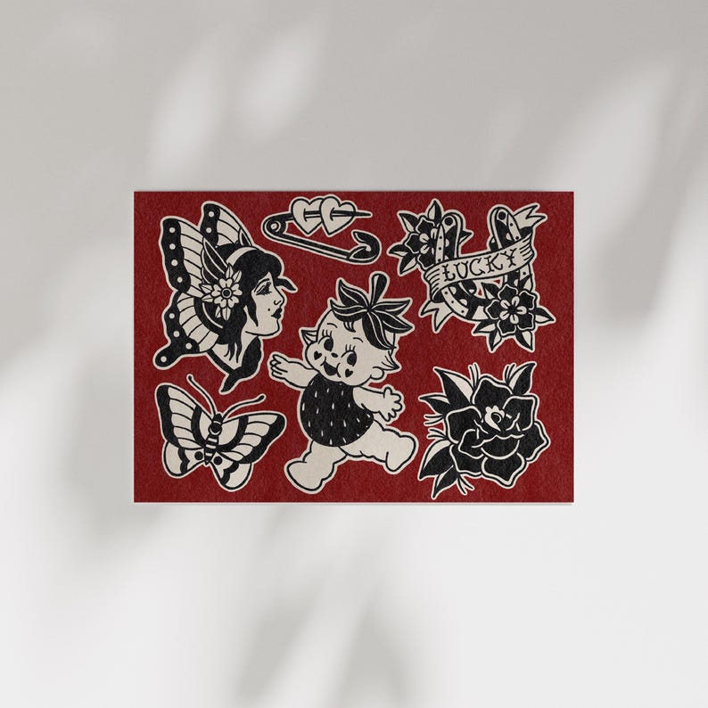 May include: A red card featuring black and white traditional tattoo designs. The designs include a butterfly, a woman's face, a baby, a safety pin with hearts, a banner that says "Lucky", and roses.