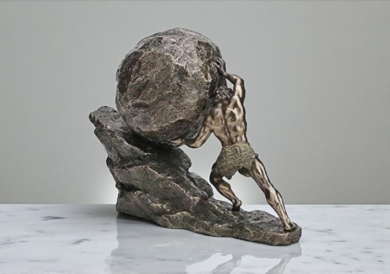 May include: Bronze sculpture depicting a muscular figure pushing a large, textured boulder uphill. The figure is clad in a loincloth, and the sculpture rests on a rocky base. The color palette is primarily bronze and brown.
