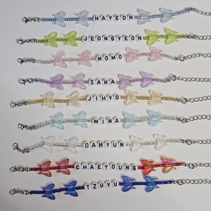 May include: A selection of beaded butterfly bracelets in various colours, each with a name spelled out in white letter beads. The bracelets have a chain closure and are displayed on a white surface.