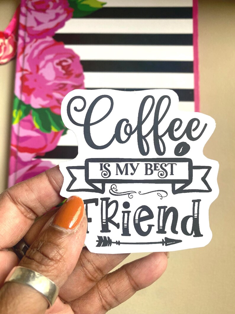 Puede incluir: Una pegatina blanca con el texto "Coffee is my best friend" en escritura negra y letras de bloque. La pegatina se sostiene frente a un cuaderno con un dise&ntilde;o floral y rayas blancas y negras.