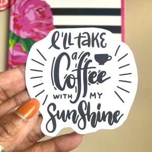 Puede incluir: Una pegatina blanca con letras negras que dice "I'll take a Coffee with my Sunshine". La pegatina tiene un gr&aacute;fico de taza de caf&eacute; y l&iacute;neas radiantes. El fondo incluye un dise&ntilde;o floral y rayas blancas y negras.