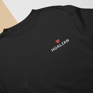 Pode incluir: Camisola de moletom preta com um coração bordado branco e o texto "HUALIAN" na frente.