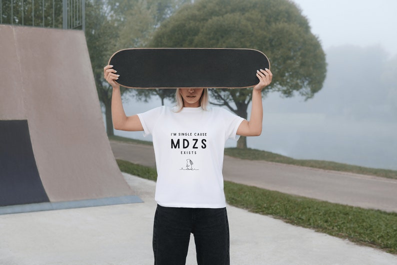 K&ouml;nnte beinhalten: Eine Person tr&auml;gt ein wei&szlig;es T-Shirt mit dem Text "I'm single cause MDZS exists" und einer Schwarzwei&szlig;illustration eines Charakters. Die Person h&auml;lt ein Skateboard &uuml;ber ihrem Kopf.