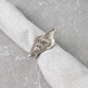 Puede incluir: Anillo de servilleta de concha de mar de plata. El anillo tiene forma de concha de mar con un diseño detallado.
