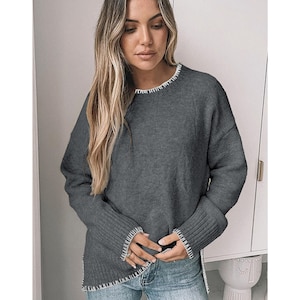 May include: A white ceramic mug with a black handle and the text "But First, Coffee" in a bold, black font. The mug is set against a blurred background, suggesting a cosy setting.