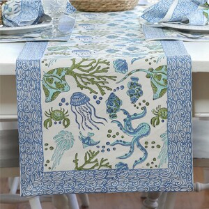 Könnte beinhalten: Ein weißer Tischläufer mit blauem Rand und einem Meereslebewesen-Muster. Das Muster umfasst Quallen, Seepferdchen, Seesterne und Korallen. Der Läufer ist perfekt für ein Esszimmer im Küsten-Stil.