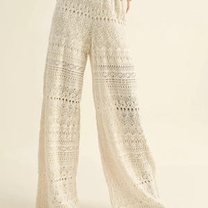 May include: Cream-coloured crochet trousers with a wide leg design. The trousers feature an open weave pattern and are paired with a matching crop top. The outfit is made of a soft, lightweight material, ideal for warmer weather.
