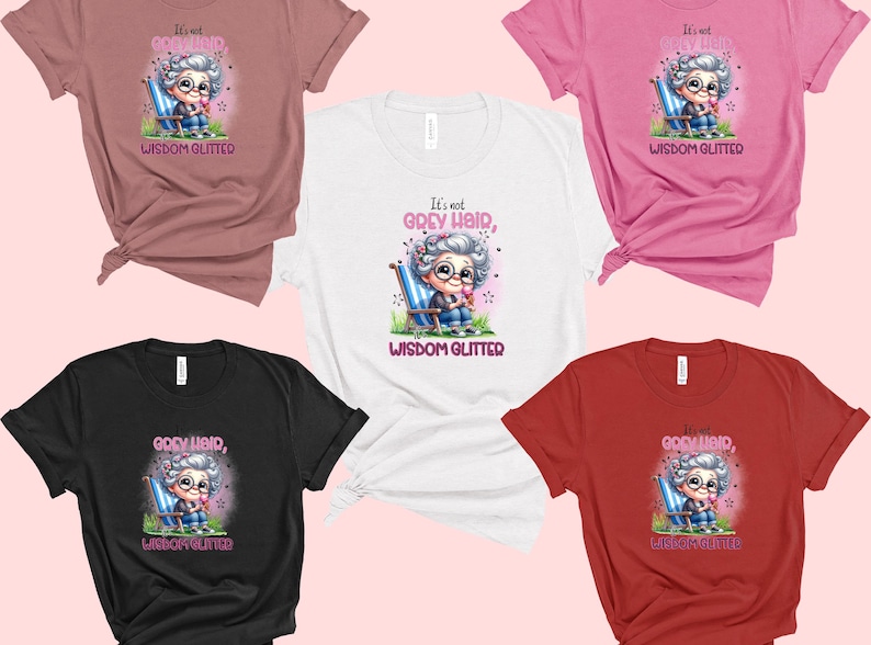 Op de afbeelding: Vijf verschillende gekleurde T-shirts met een afbeelding van een cartoon oma die op een stoel zit met de tekst "Het is geen grijs haar, wijsheid glinstert".