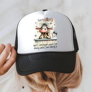 May include: A black and white trucker hat with a white front panel featuring a cartoon donkey graphic. The donkey is resting its chin on a ledge, with the text "Not to BRAG but I can forget what I'm doing while I am doing it."