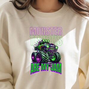 May include: A white sweatshirt featuring a green and purple monster truck graphic with the text "Monster Trucks Are My Jam".
