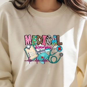 May include: A white sweatshirt with a colorful graphic design that says "MEDICAL Records" with a stethoscope, syringe, and clipboard.
