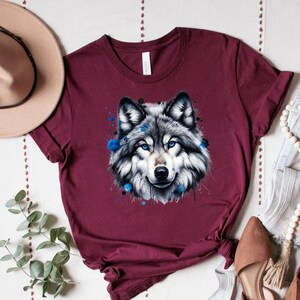 May include: A maroon t-shirt with a watercolor design of a wolf's head with blue accents.