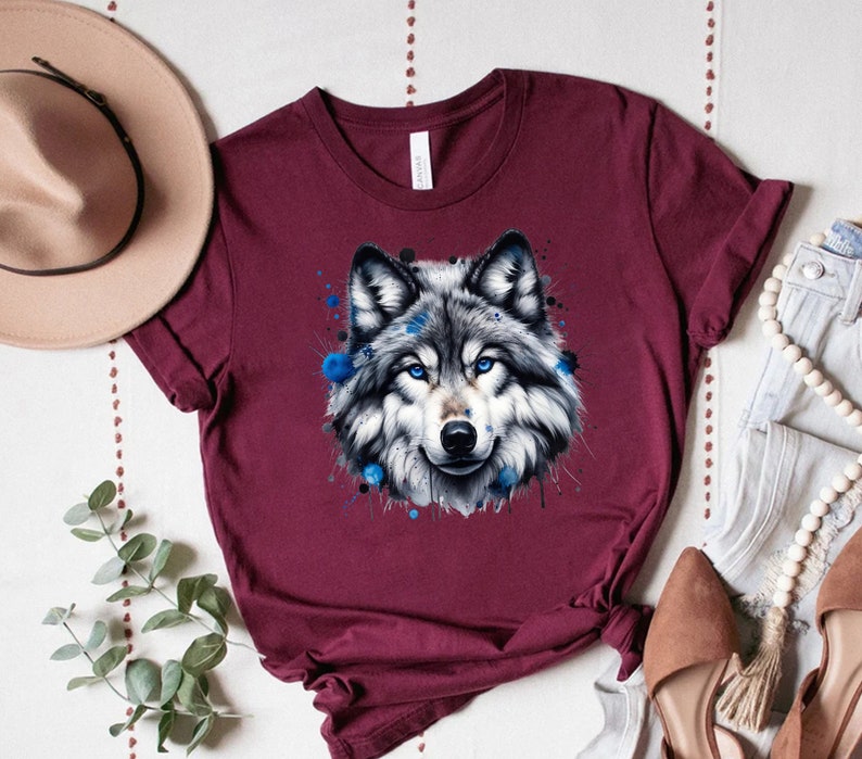 May include: A maroon t-shirt with a watercolor design of a wolf's head with blue accents.