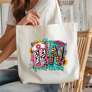 May include: A white canvas tote bag with a colorful graphic design featuring the letters "RN" with a leopard print pattern, a nurse's hat, a stethoscope, a syringe, and sunflowers. The text "You good hands" is printed below the graphic.