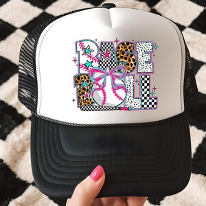 May include: A white and black trucker hat with a colorful baseball graphic that says "BASEBALL" with a pink bow and a baseball. The hat has a black mesh back.