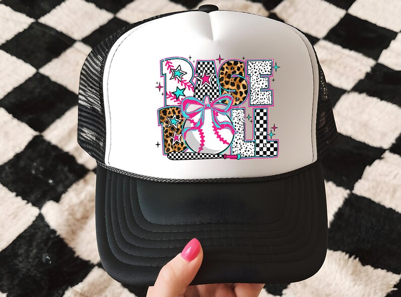 May include: A white and black trucker hat with a colorful baseball graphic that says "BASEBALL" with a pink bow and a baseball. The hat has a black mesh back.