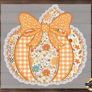May include: A decorative pumpkin design with an orange bow and a white lace trim. The pumpkin features a gingham pattern and floral accents in orange, blue, and white. The background is a gray wood grain.