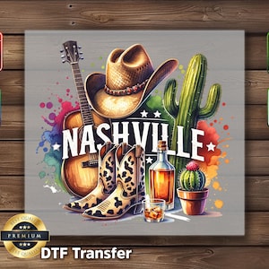 May include: Watercolor illustration featuring a cowboy hat, guitar, and boots with the word "Nashville." Includes a cactus, whiskey bottle, and glass. The design is a DTF transfer.
