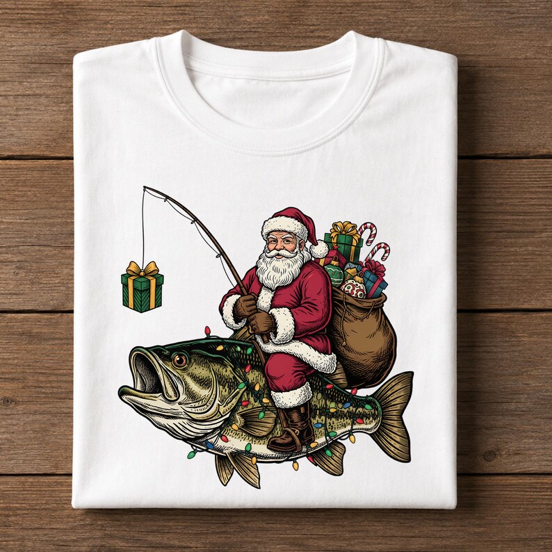 May include: A white t-shirt featuring a graphic of Santa Claus riding a large bass fish. Santa wears a red suit and carries a brown sack filled with gifts. He holds a fishing rod with a green gift box on the line. The fish is decorated with colorful Christmas lights.