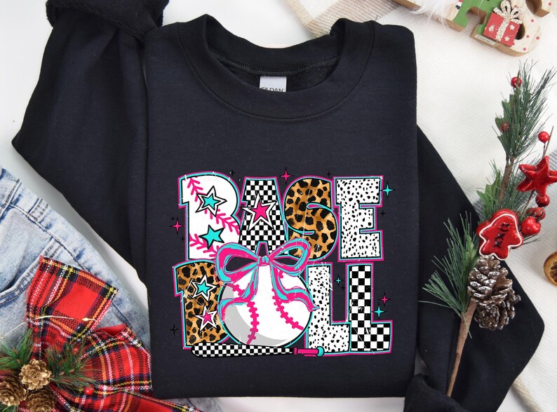 May include: Black sweatshirt with a graphic design of a baseball with a bow and the word "BASEBALL" in a colorful, patterned font.