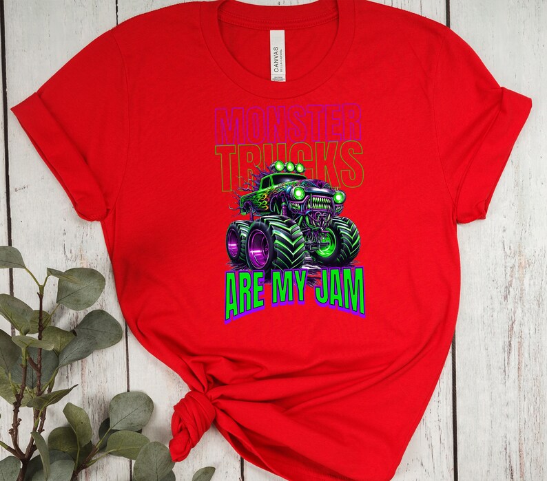 May include: Red t-shirt featuring a green and black monster truck graphic with the text "Monster Trucks Are My Jam".