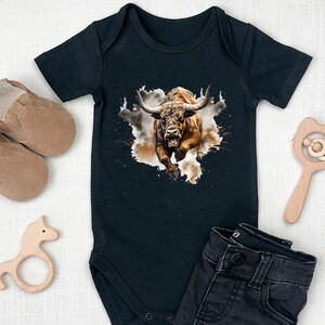 May include: Black baby onesie with a brown bull graphic. The bull is charging with its horns forward and mouth open. The bull is on a white background with brown splatters.