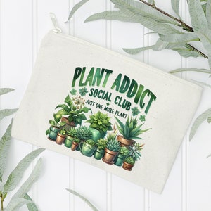 May include: A white canvas zippered pouch with the text "Plant Addict Social Club Just One More Plant" and a colourful illustration of various potted plants.