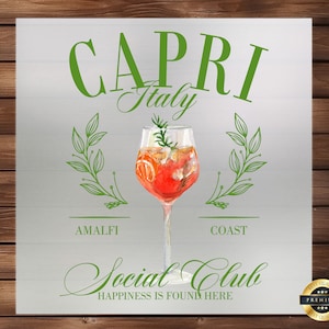 May include: A watercolor illustration of a cocktail glass with a drink, a sprig of rosemary, and orange slices. The text "CAPRI Italy" is above the glass, and "AMALFI COAST" is below the glass. The text "Social Club" is below the glass with the text "HAPPINESS IS FOUND HERE" below that. A gold seal with the text "BEST QUALITY" and "PREMIUM" is in the lower right corner.