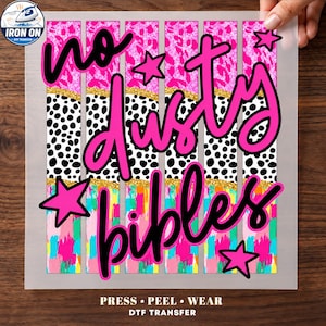 May include: A DTF iron-on transfer sheet featuring vertical stripes with pink leopard print, black and white dalmatian spots, and colorful brushstrokes, separated by gold glitter lines. The text reads no dusty bibles in black script with pink stars.