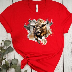 May include: Red t-shirt with a graphic of a brown bull charging through a cloud of dust and paint splatters.