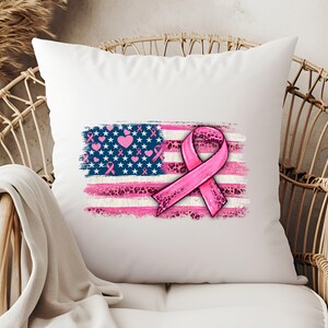 May include: White pillow with a pink ribbon and an American flag design. The flag is distressed and has pink hearts and ribbons on it. The ribbon is pink with a leopard print pattern.