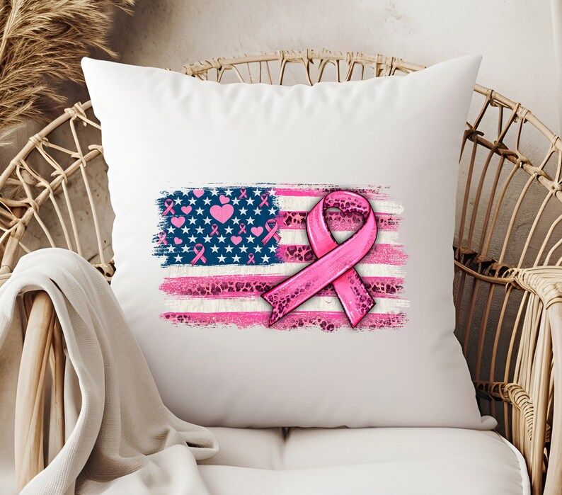 May include: White pillow with a pink ribbon and an American flag design. The flag is distressed and has pink hearts and ribbons on it. The ribbon is pink with a leopard print pattern.