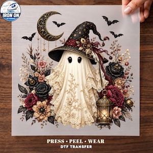 May include: A DTF transfer sheet featuring a ghost wearing a black witch hat with gold stars, surrounded by dark red and black flowers, bats, and a crescent moon. A lit lantern hangs from the ghost, with the text PRESS PEEL WEAR DTF TRANSFER.