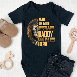 May include: Black baby onesie with a lion graphic and the text "Man of God Husband Daddy Protector Hero".