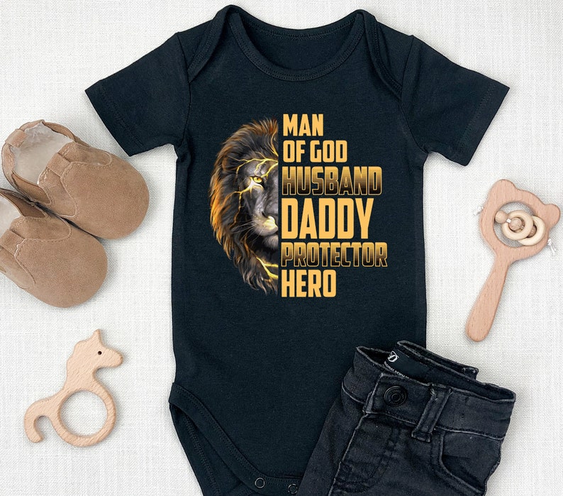 May include: Black baby onesie with a lion graphic and the text "Man of God Husband Daddy Protector Hero".