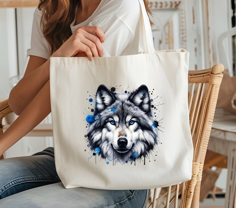 May include: A white canvas tote bag with a watercolor illustration of a wolf's face. The wolf has blue eyes and is surrounded by blue paint splatters.