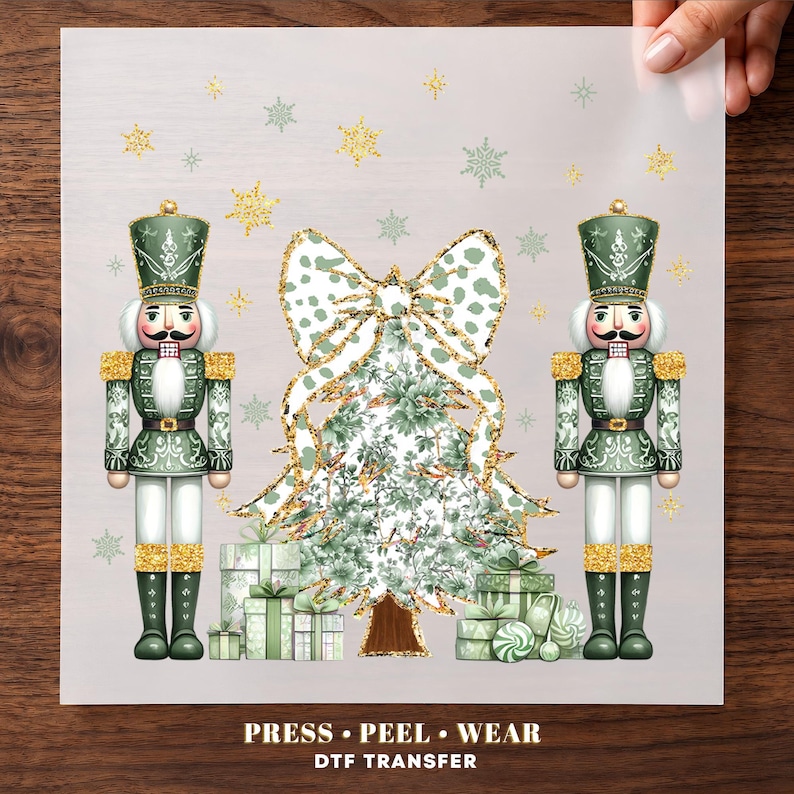 May include: A DTF transfer sheet featuring two green nutcrackers flanking a central Christmas tree topped with a large green and white patterned bow. The design includes gold glitter accents, stacked gift boxes, and snowflakes. Text reads: PRESS PEEL WEAR DTF TRANSFER.