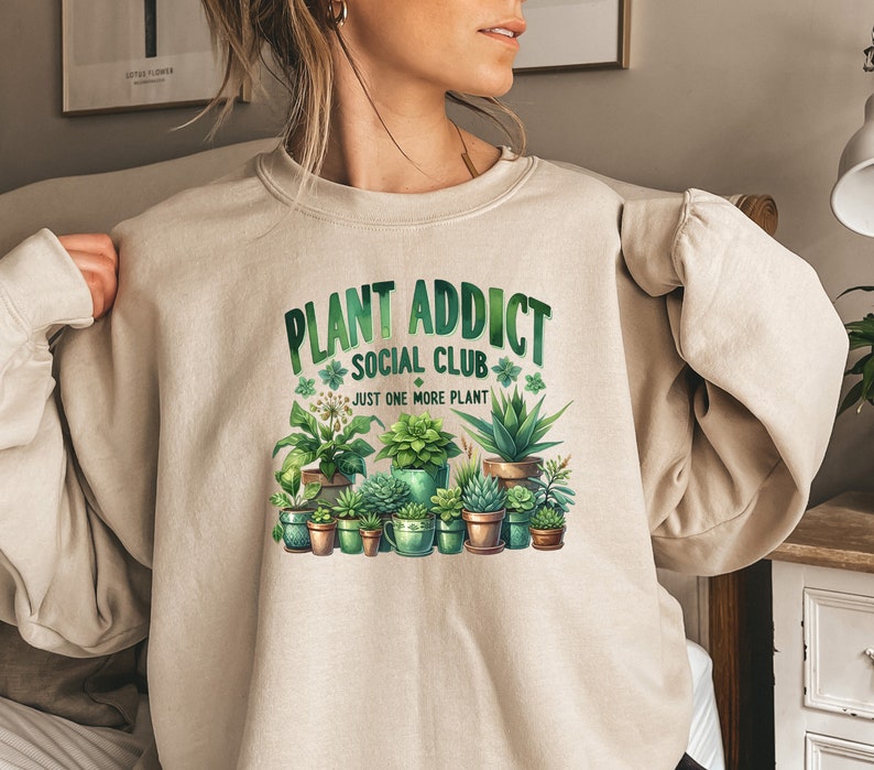 May include: A beige sweatshirt with the text "Plant Addict Social Club" and a graphic of potted plants. The text below the graphic says "Just one more plant."