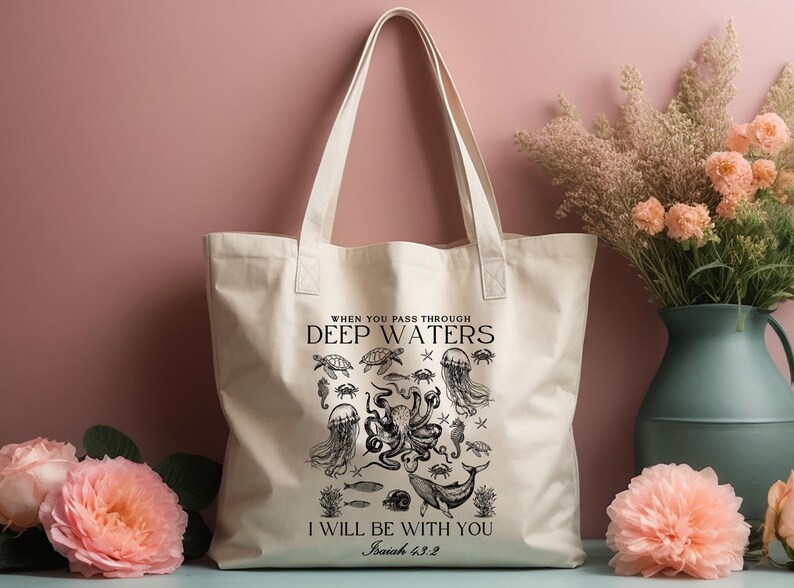 May include: Cream-colored tote bag featuring a black illustration of sea creatures, including an octopus, jellyfish, and whale. The text reads "WHEN YOU PASS THROUGH DEEP WATERS I WILL BE WITH YOU Isaiah 43:2".