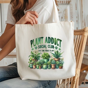 May include: A white canvas tote bag with the text "Plant Addict Social Club" and the phrase "Just One More Plant". The bag features a colourful illustration of various potted plants.