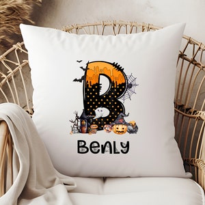 May include: White square pillow with a Halloween-themed design. The letter "B" is decorated with orange dripping paint, black polka dots, and Halloween imagery. The name "Benly" is printed below the letter.