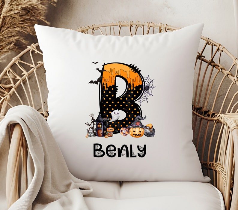 May include: White square pillow with a Halloween-themed design. The letter "B" is decorated with orange dripping paint, black polka dots, and Halloween imagery. The name "Benly" is printed below the letter.