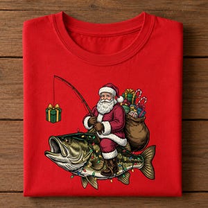 May include: A bright red t-shirt featuring a graphic of Santa Claus riding a large fish. Santa holds a fishing rod with a green gift box on the line. A brown sack filled with colorful presents sits behind Santa, and the fish is decorated with lights.