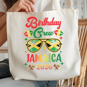 A white tote bag with a colorful graphic design featuring sunglasses, a Jamaican flag, and text that says "Birthday Crew Jamaica 2026".
