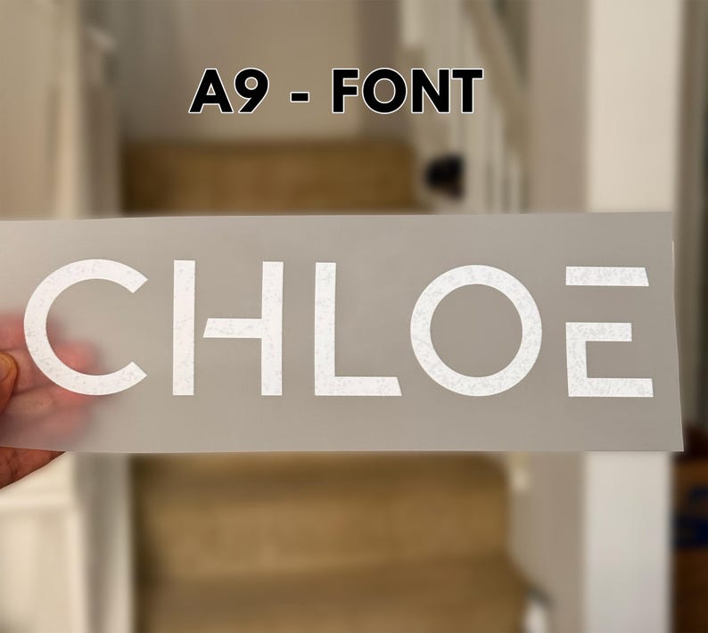 May include: A rectangular, semi-transparent transfer sheet featuring the white text CHLOE in a modern, sans-serif font. The letters have a subtle, speckled texture. Above the sheet, the text A9 - FONT is displayed in black against a blurred background.