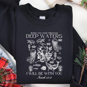 May include: Black sweatshirt with a white graphic of various sea creatures, including an octopus, jellyfish, and whale. The text reads "When you pass through deep waters, I will be with you, Isaiah 43:2."