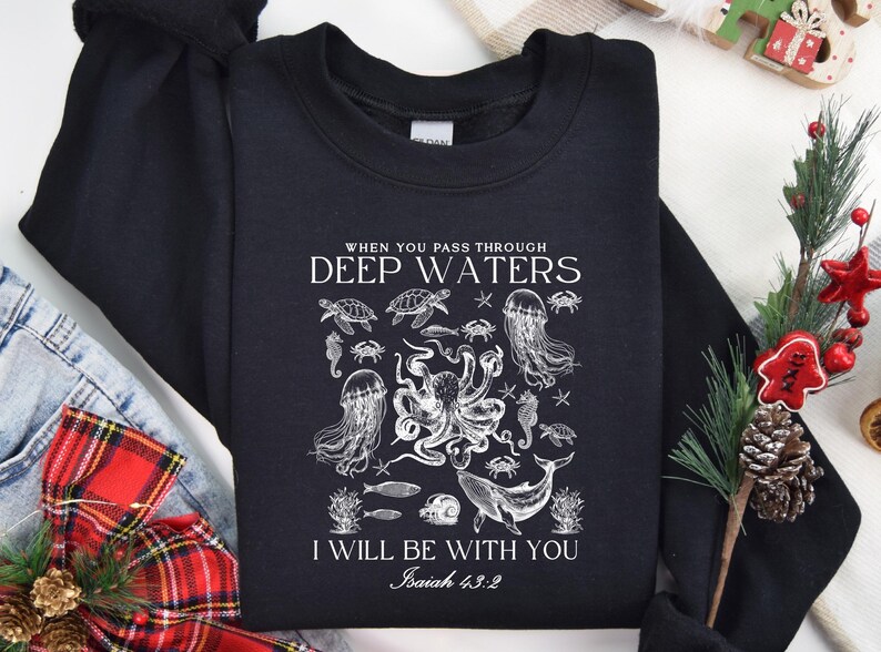 May include: Black sweatshirt with a white graphic of various sea creatures, including an octopus, jellyfish, and whale. The text reads "When you pass through deep waters, I will be with you, Isaiah 43:2."